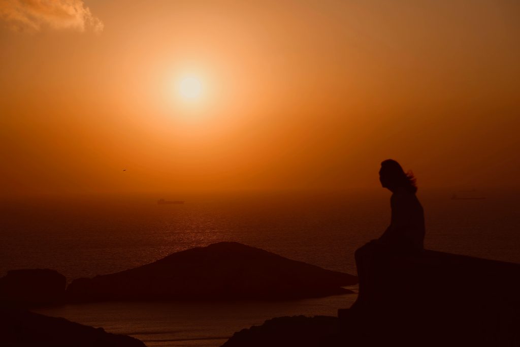Person reflecting by the ocean at sunrise, symbolizing resilience and hope during global conflict.