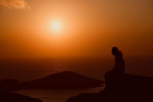 Person reflecting by the ocean at sunrise, symbolizing resilience and hope during global conflict.